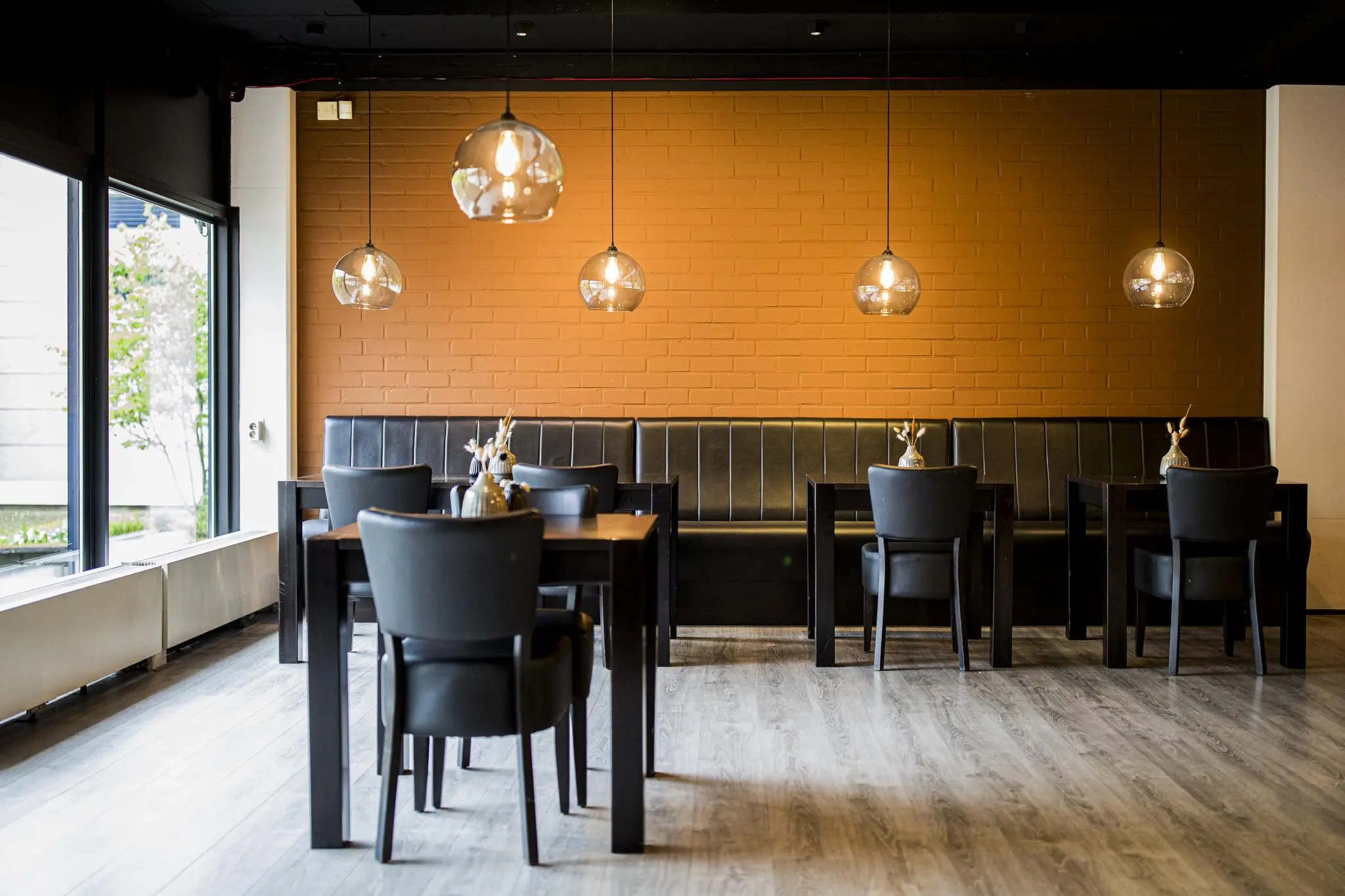Modern ingerichte zithoek in restaurant Markerkant 13 met zwarte stoelen, houten tafels en hanglampen voor een oranje bakstenen muur.
